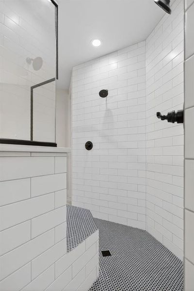 Spacious walk-in shower featuring white subway tile walls, a built-in bench with mosaic tile, and dark circular mosaic floor tiling Spacious walk-in shower featuring white subway tile walls, a built-in bench with mosaic tile, and dark circular mosaic floor tiling