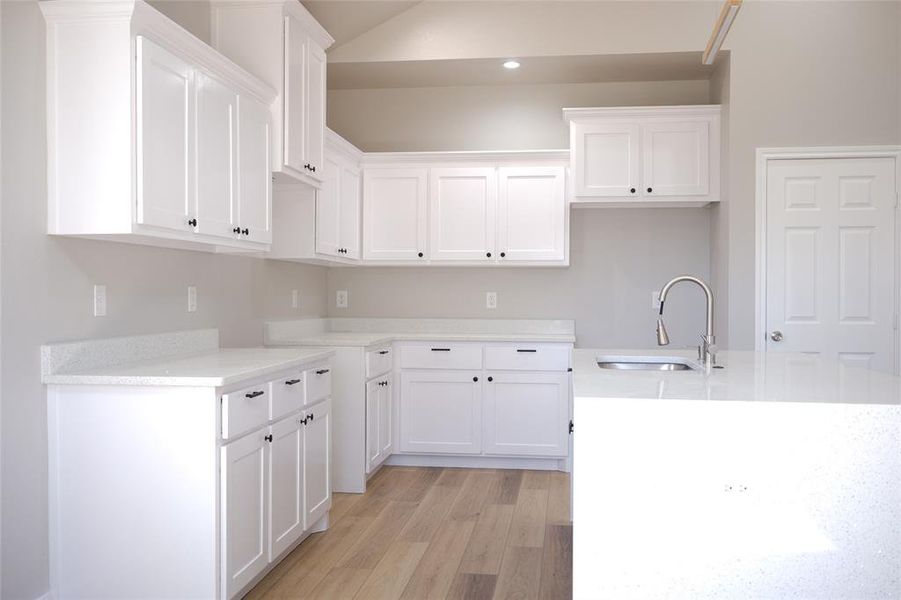 Kitchen with white cabinets, light stone countertops, light wood finished floors, and lofted ceiling Kitchen with white cabinets, light stone countertops, light wood finished floors, and lofted ceiling