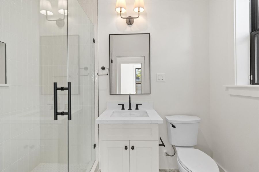 This bathroom is crisp and modern with a sleek vanity, quartz countertop, and matte black fixtures that add contrast. The glass-enclosed shower keeps the space feeling open while the clean tilework and well-placed lighting give it a fresh, hotel-style finish.