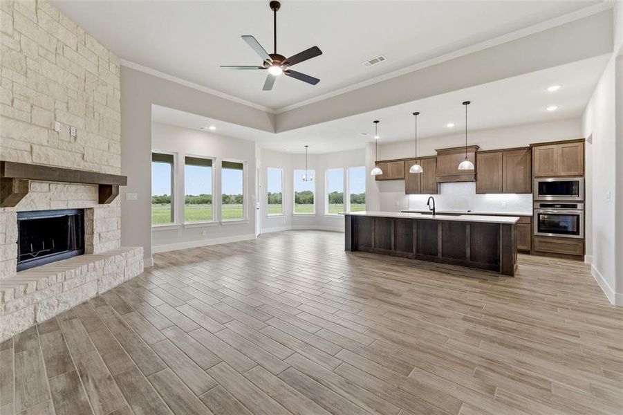 Open-concept living space featuring wood-finish flooring, a stone-faced fireplace with a wood mantle, and a kitchen island with pendant lighting