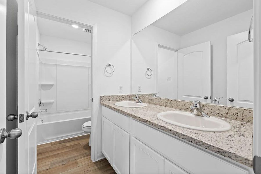 Secondary bathroom includes double vanities, granite counters, designer white cabinetry and luxury vinyl plank flooring.