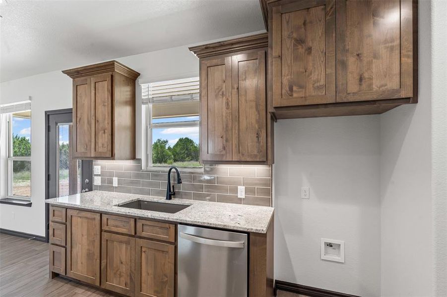 Kitchen featuring decorative backsplash, stainless steel dishwasher, light stone counters, and wood finished floors