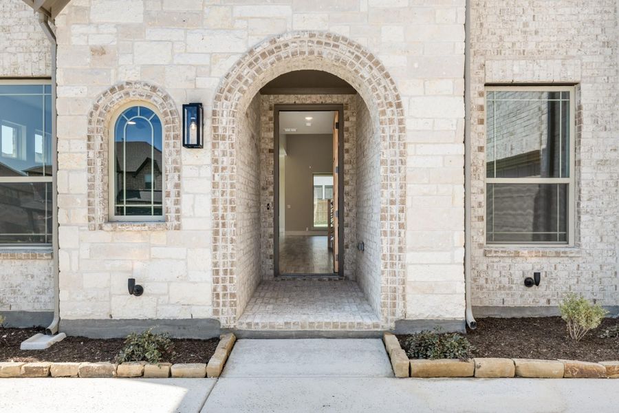 Home entrance with arched brick surround, open front door, and concrete walkway leading inside.