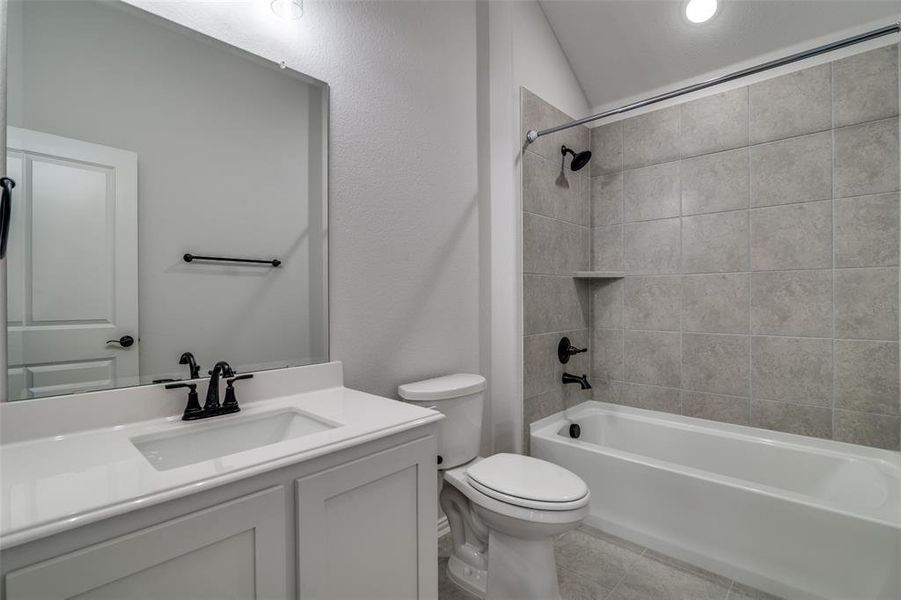 Full bathroom upstairs, featuring toilet, vanity, lofted ceiling, and tiled shower / bath