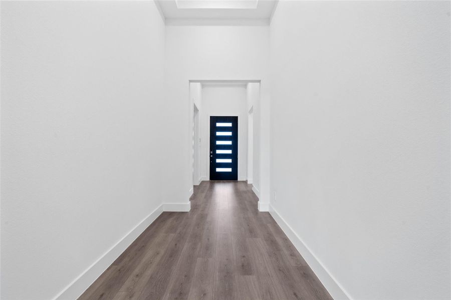 This striking entry makes a bold first impression, featuring an extra-wide hallway with contemporary laminate flooring. The clean, all-white walls and high ceilings create a bright and airy atmosphere, perfectly setting a modern tone for the rest of the home.