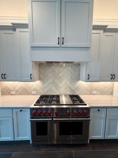 A professional gas range anchors this culinary workspace featuring a herringbone tile backsplash.