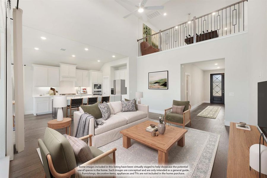 Open-concept living room with two-story ceiling, ceiling fan, and kitchen visible in background Open-concept living room with two-story ceiling, ceiling fan, and kitchen visible in background