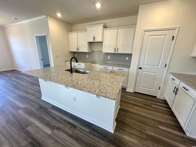 Kitchen featuring white cabinets, granite countertops, beautiful backsplash, an island with sink, and dark wood finished floors Kitchen featuring white cabinets, granite countertops, beautiful backsplash, an island with sink, and dark wood finished floors