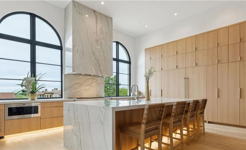 Kitchen featuring light brown cabinetry, light stone countertops, modern cabinets, a kitchen breakfast bar, and light wood finished floors