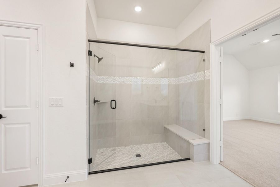 Walk-in shower with glass door, built-in bench, white tile walls, and black hardware fixtures