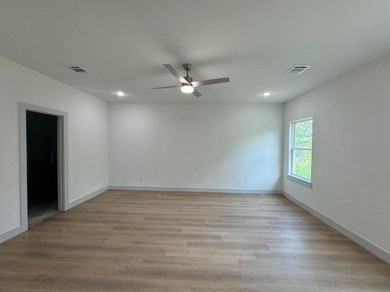 This is a spacious, well-lit room with modern wood flooring, neutral walls, and a ceiling fan. It features recessed lighting and has at least one window that provides natural light.