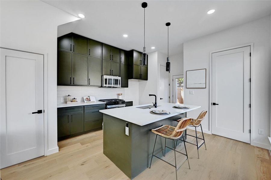 Kitchen with pendant lighting, light hardwood / wood-style floors, sink, a kitchen breakfast bar, and a center island with sink