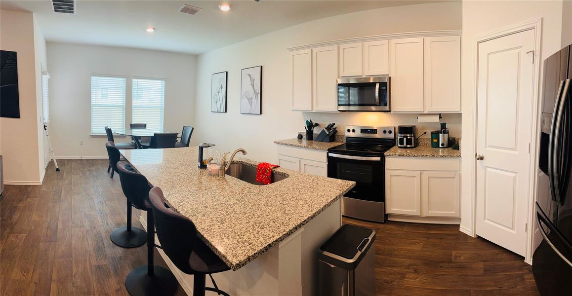 Open-concept kitchen featuring an island with a stainless steel appliances, granite countertops, white cabinetry, and wood-finish flooring. Open-concept kitchen featuring an island with a stainless steel appliances, granite countertops, white cabinetry, and wood-finish flooring.