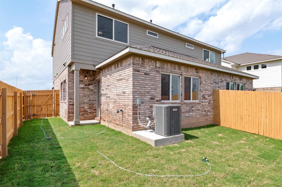 Rear view of house featuring brick siding, central AC unit, a fenced backyard, and a yard