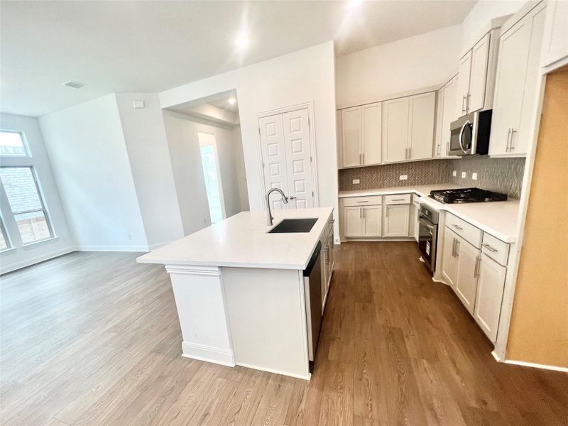 Kitchen featuring tasteful backsplash, light countertops, a kitchen island with sink, appliances with stainless steel finishes, and light wood-type flooring Kitchen featuring tasteful backsplash, light countertops, a kitchen island with sink, appliances with stainless steel finishes, and light wood-type flooring