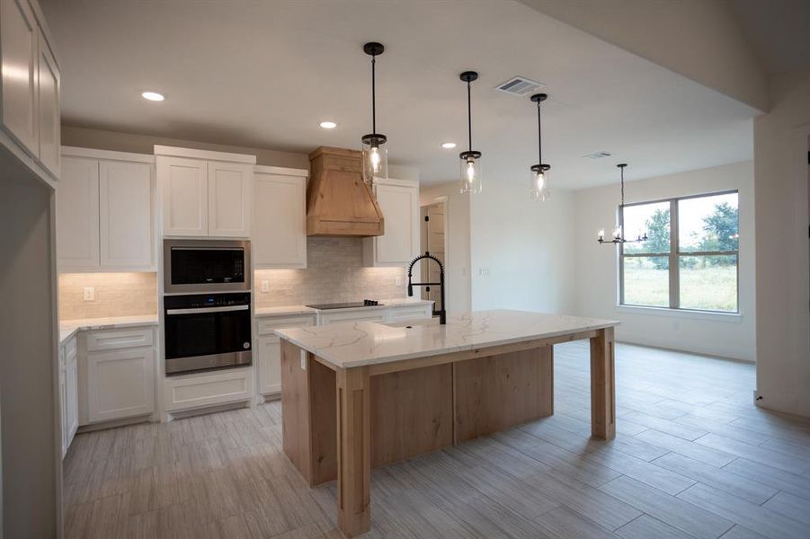 Kitchen with tasteful backsplash, oven, light stone counters, white cabinets, and pendant lighting Kitchen with tasteful backsplash, oven, light stone counters, white cabinets, and pendant lighting