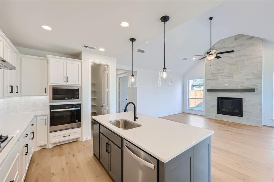 Kitchen with sink, stainless steel appliances, white cabinets, light hardwood / wood-style flooring, and a center island with sink