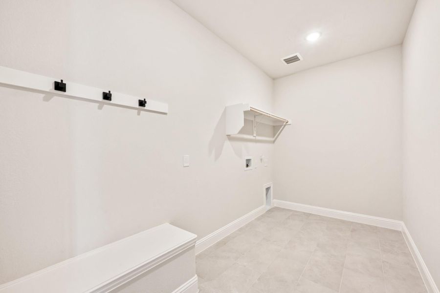 Laundry room with white walls, tile floor, wall shelf, washer hookups, and a mudroom bench with black coat hooks. Laundry room with white walls, tile floor, wall shelf, washer hookups, and a mudroom bench with black coat hooks.