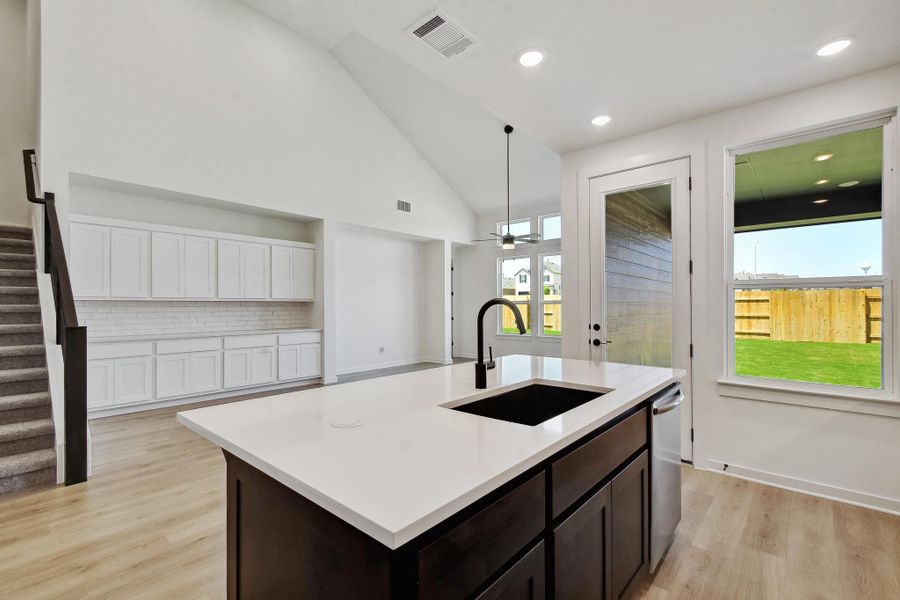 Kitchen with light wood-style flooring, light countertops, dark brown cabinetry, decorative backsplash, and pendant lighting