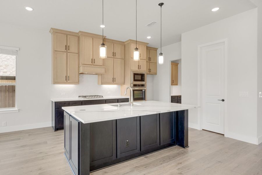 Kitchen with dark island, white countertops, light wood cabinets, pendant lights, and hardwood floors Kitchen with dark island, white countertops, light wood cabinets, pendant lights, and hardwood floors