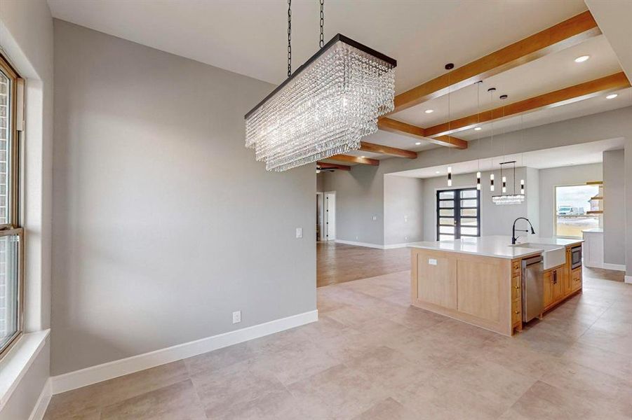 Kitchen featuring pendant lighting, beamed ceiling, light brown cabinetry, a large island, and sink