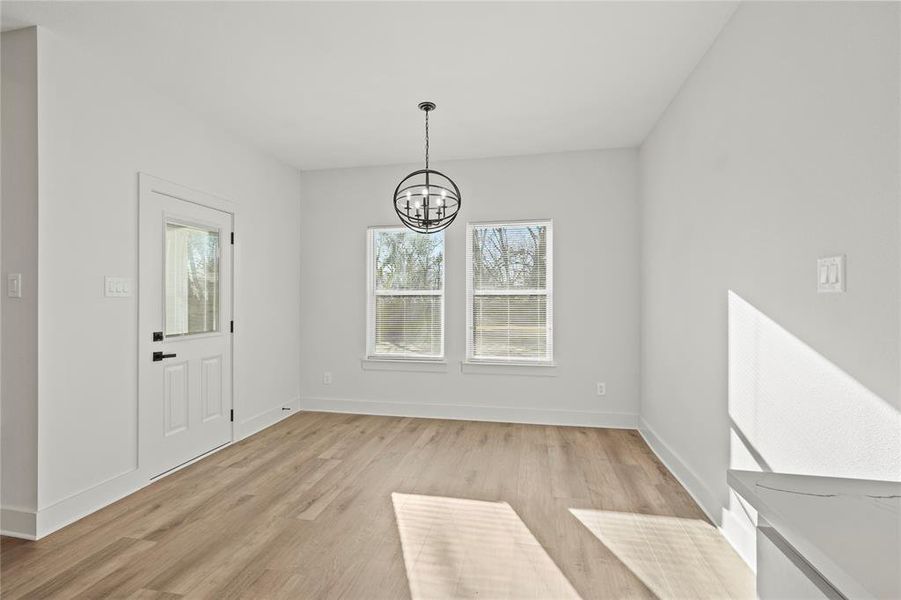 Unfurnished dining area with light wood finished floors, baseboards, and a notable chandelier