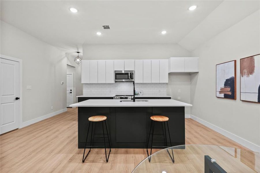 Kitchen featuring decorative backsplash, light wood-type flooring, a center island with sink, and white cabinetry