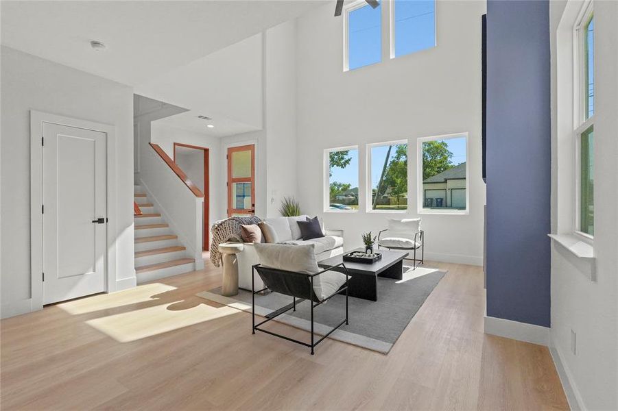 Living room with light wood finished floors, a towering ceiling, and stairway Living room with light wood finished floors, a towering ceiling, and stairway