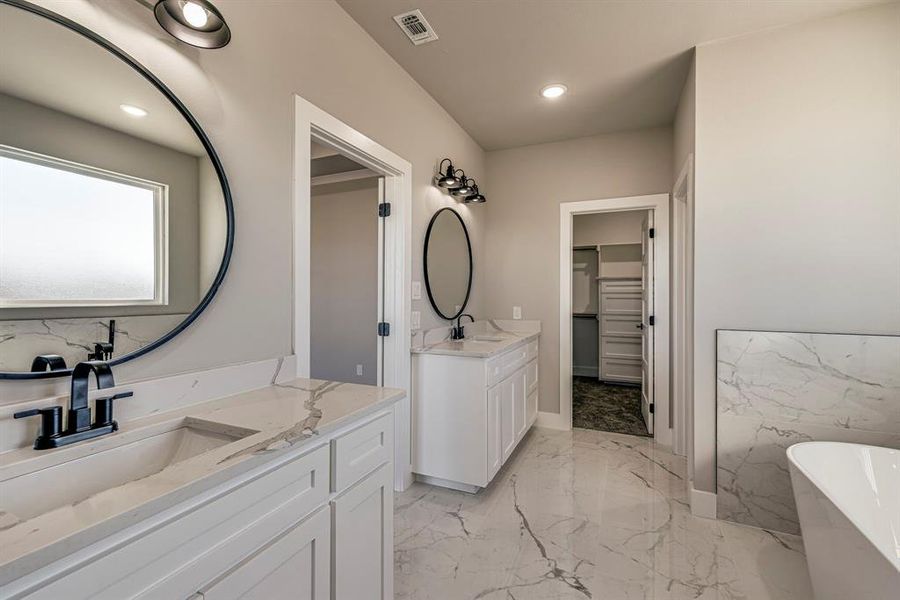 Bathroom featuring visible vents, a soaking tub, two vanities, a spacious closet, and marble finish floor