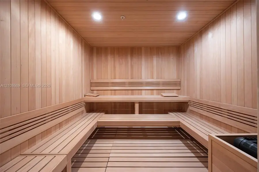 Sauna featuring wood paneling, multi-level built-in bench seating, recessed lighting, and a slatted wood floor