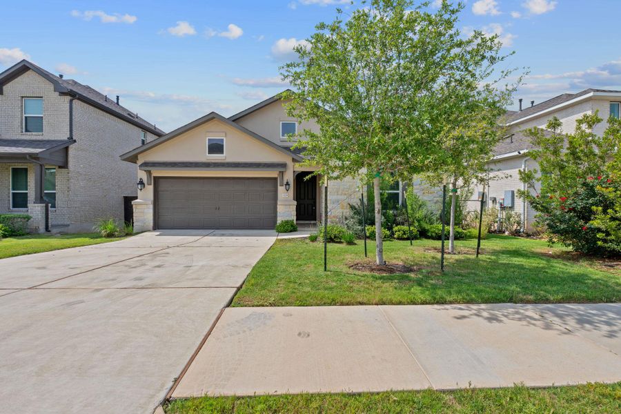 View of front of house with an attached garage, stone siding, a front yard, concrete driveway, and stucco siding