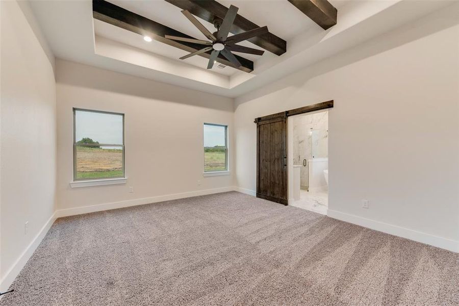 Unfurnished bedroom with a barn door, carpet, ensuite bathroom, ceiling fan, and beamed ceiling Unfurnished bedroom with a barn door, carpet, ensuite bathroom, ceiling fan, and beamed ceiling