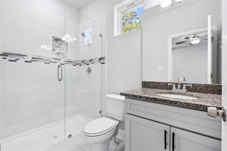 Bathroom with walk in shower, ceiling fan, vanity, and toilet