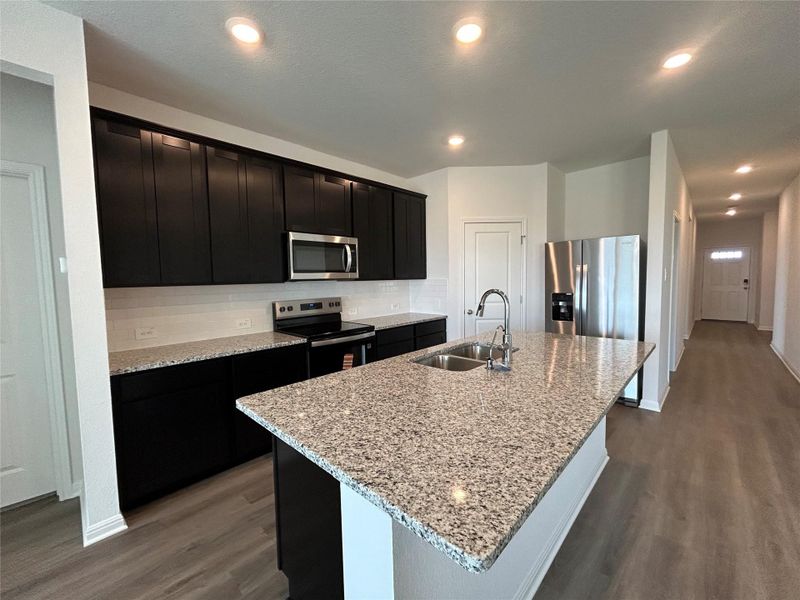 Kitchen with backsplash, light stone counters, stainless steel appliances, dark wood-style flooring, and an island with sink Kitchen with backsplash, light stone counters, stainless steel appliances, dark wood-style flooring, and an island with sink