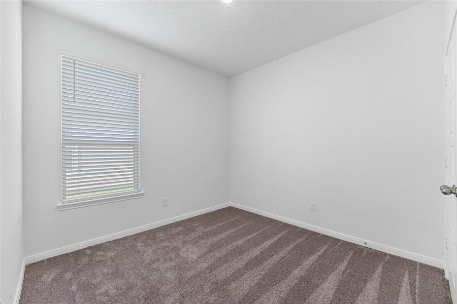 Secondary bedroom features plush carpet flooring, neutral paint, lighting, large window with privacy blinds, and an ample sized closet space.