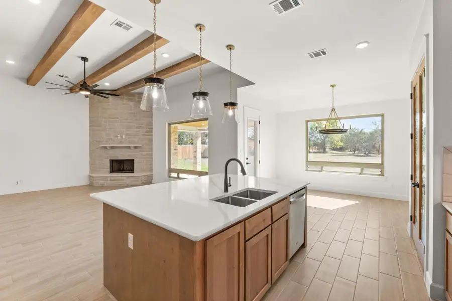 Kitchen featuring brown cabinetry, pendant lighting, wood tiled floors, a stone fireplace, and an island with sink