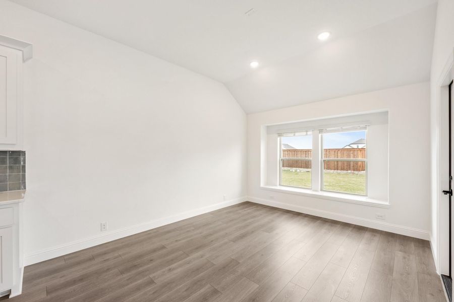 Empty room with vaulted ceiling, gray wood floors, and large window overlooking backyard