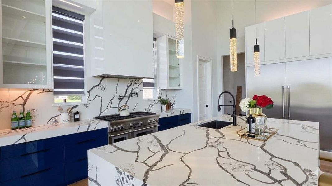 Gourmet kitchen featuring a large central island, patterned stone countertops and backsplash, professional-grade range, stainless steel French door refrigerator, and custom blue and white cabinetry