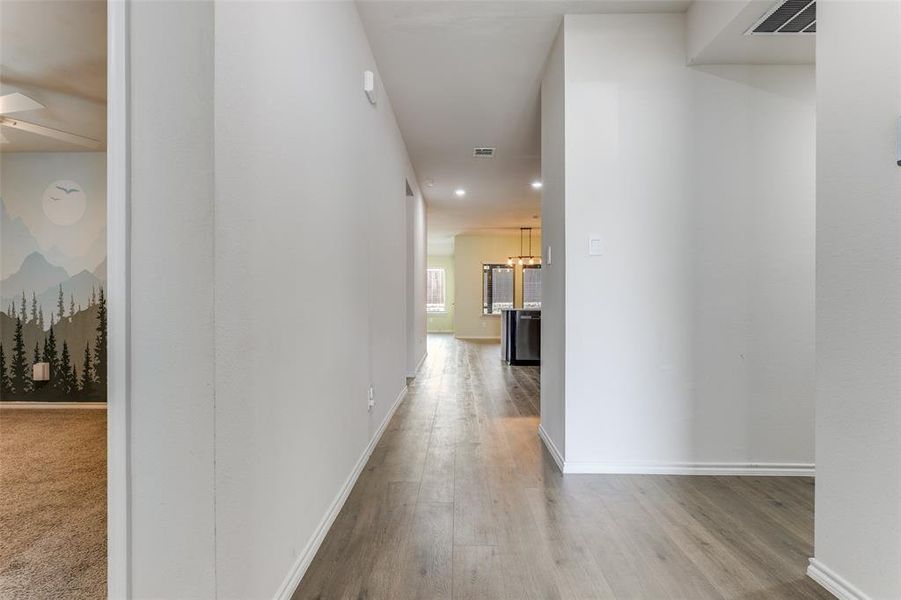 Hallway featuring light wood-finish flooring, white baseboards, and neutral wall tones Hallway featuring light wood-finish flooring, white baseboards, and neutral wall tones
