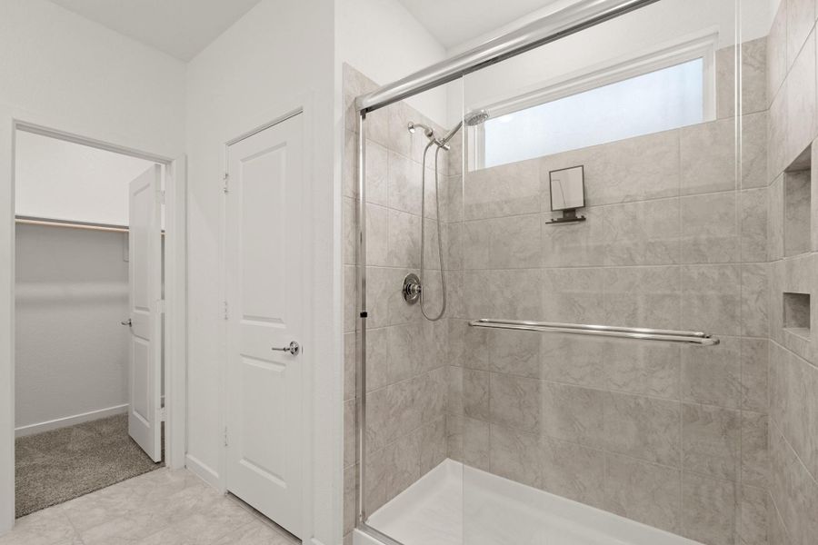The primary bathroom has a walk-in shower with tile surround, glass door and window letting in natural light.