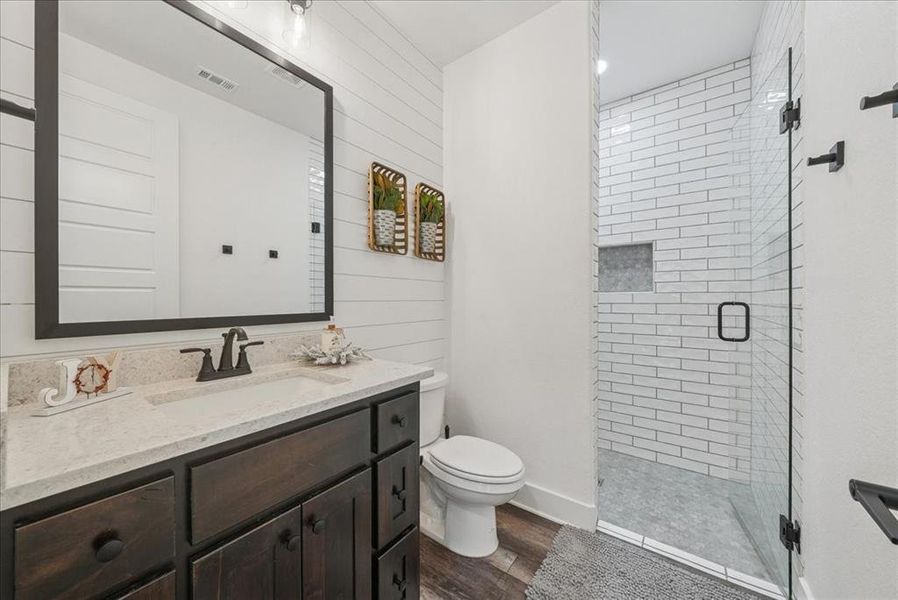 Full bath with a shower stall, vanity, dark wood-type flooring, and wood walls
