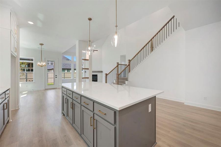Kitchen featuring hanging lights, a kitchen island, a glass covered fireplace, light wood finished floors, and open floor plan