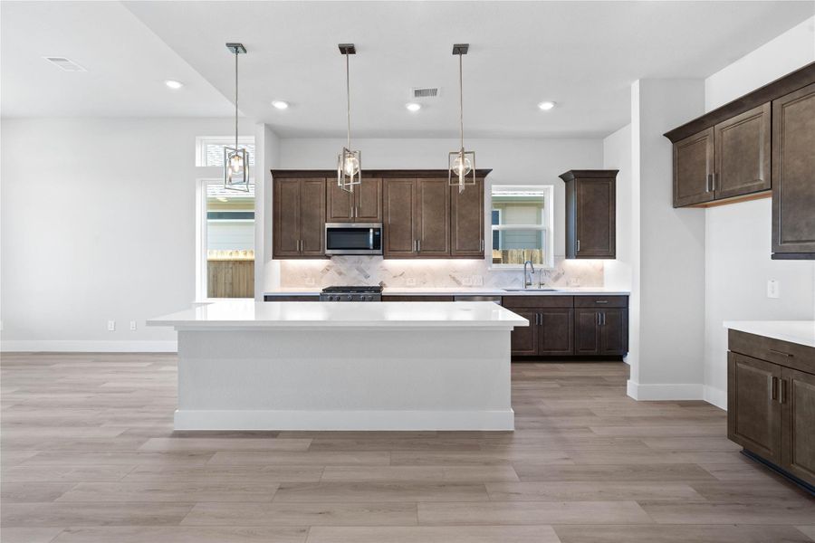 The kitchen anchors the space with warm, dark wood cabinetry, stainless steel appliances, sleek white quartz countertops, and a large island perfect for casual dining or hosting.