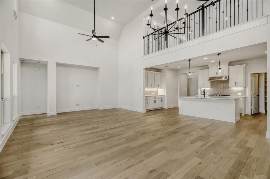 Unfurnished living room featuring a ceiling fan, a high ceiling, light wood finished floors, and a chandelier