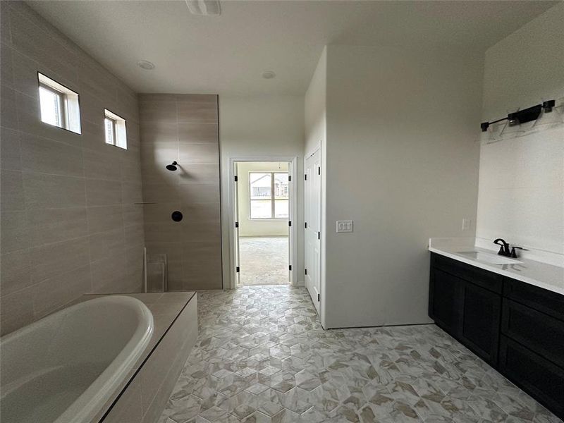 Full bathroom featuring vanity, a garden tub, tiled shower, and light stone finish floors