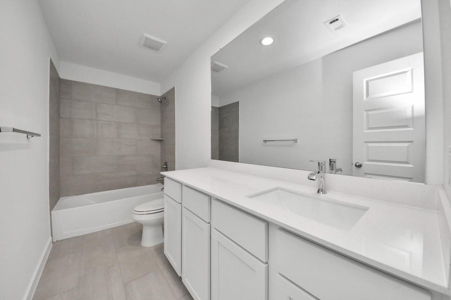 Secondary bath features tile flooring, bath/shower combo with tile surround, light stained wood cabinets, beautiful light countertop. Sample photo of completed home with similar floor plan. Actual colors and selections may vary.