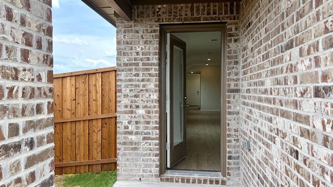 Entryway featuring brick exterior, a substantial wooden privacy fence, wood-finish flooring, recessed lighting, and a durable glass-paneled door