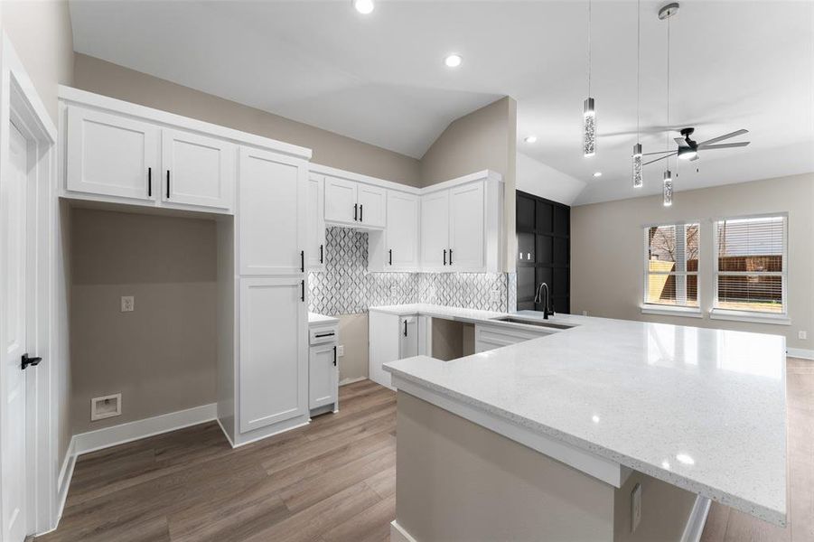 Kitchen with pendant lighting, lofted ceiling, sink, white cabinetry, and light stone counters