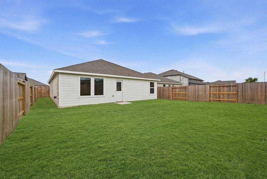This photo shows a spacious backyard with a well-maintained lawn, surrounded by a wooden fence. The house features a light exterior with large windows and a door leading to the yard, ideal for outdoor activities and gatherings.