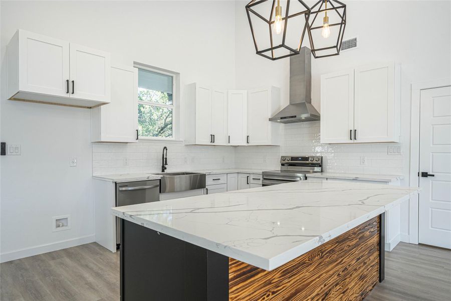 Kitchen with white cabinetry, a center island, wall chimney exhaust hood, decorative light fixtures, and appliances with stainless steel finishes